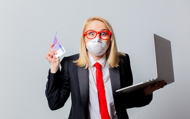Empresária em máscara facial e óculos vermelhos com dinheiro e notebook