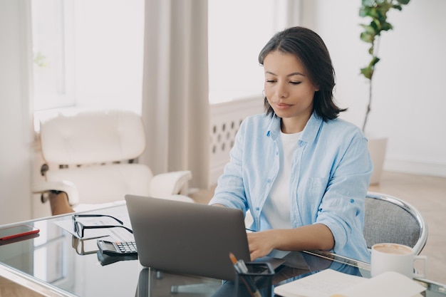 Empresaria empresaria que trabaja en línea escribiendo correo electrónico en una computadora portátil sentada en el escritorio de la oficina
