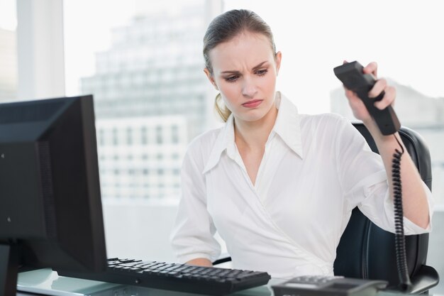 Empresaria enojada que se sienta en el escritorio que cuelga el teléfono