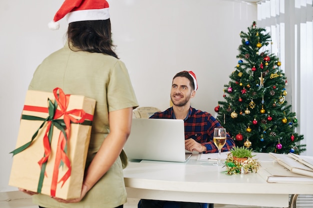 Empresária escondendo um presente de Natal para uma colega empolgada pelas costas