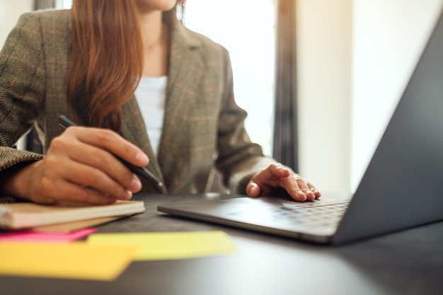 Empresária escrevendo na papelada enquanto digita no laptop sobre a mesa do escritório