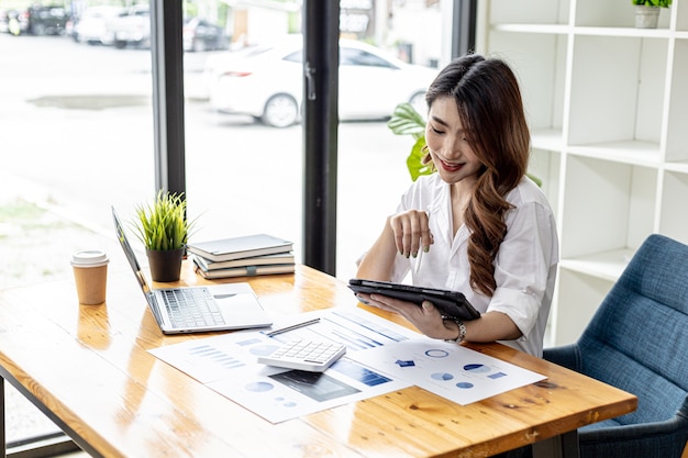 La empresaria está usando una tableta para buscar información y chatear, es dueña de un negocio y dirige a los empleados a través de un mensajero de tableta. Concepto de mujer de negocios asiática y uso de tecnología.