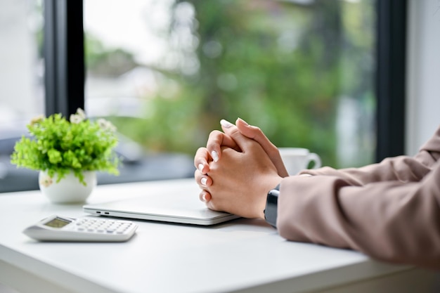 Empresária estressada e séria senta-se à mesa com as mãos juntas na mesa