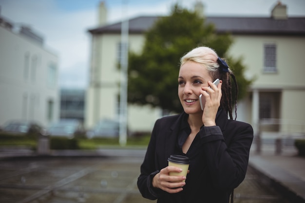 Empresária, falando no celular, segurando a xícara de café descartável