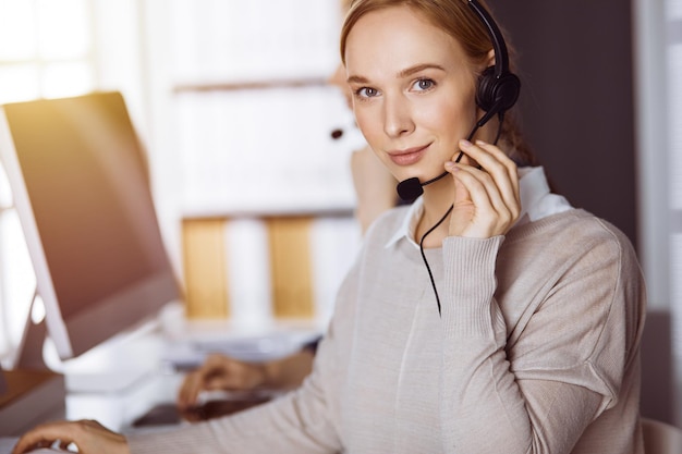 Empresária falando pelo fone de ouvido no escritório ensolarado. Call center e grupo diversificado de pessoas nos negócios.