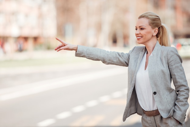 Empresaria feliz con la mano levantada para un taxi.