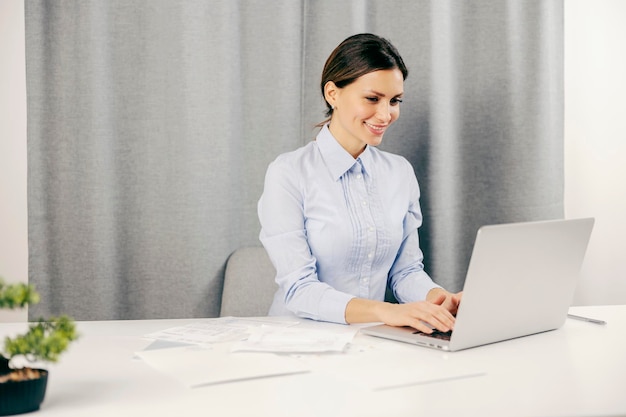 Una empresaria feliz trabajando en escribir en la computadora portátil en su oficina en casa