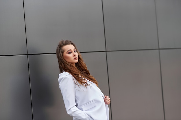 La empresaria se para frente a una pared con un traje blanco