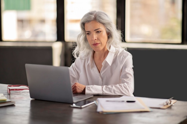 Empresária hispânica usando laptop gerenciando orçamentos on-line no escritório moderno