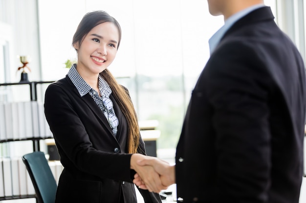 La empresaria y el hombre de negocios asiáticos se dan la mano en la sala de la oficina después de que se firma el contrato o el acuerdo de saludo de apretón de manos, el negocio expresó confianza y un concepto exitoso