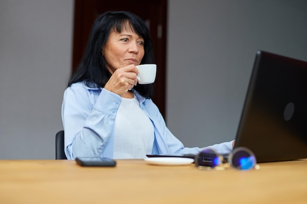 Empresária idosa relaxando no local de trabalho bebendo café