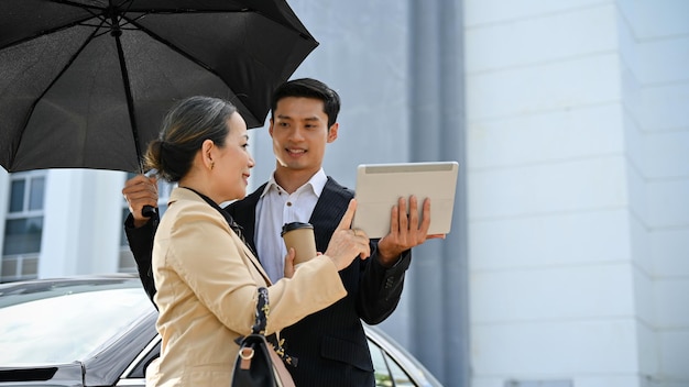 Empresária idosa verificando o trabalho no tablet digital com seu assistente masculino sob o guarda-chuva