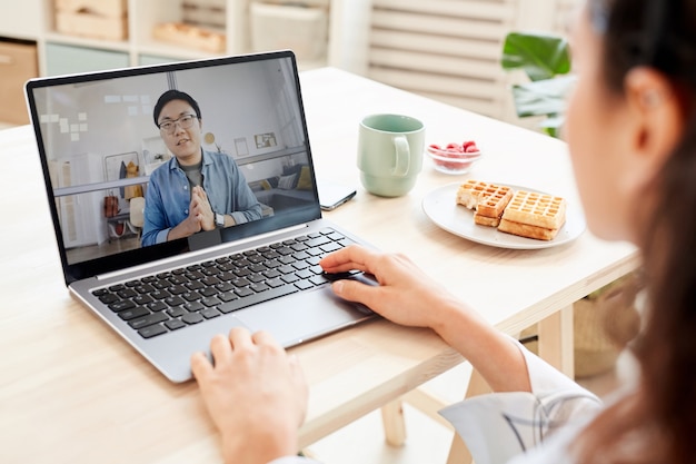 Empresaria irreconocible que trabaja con un hombre asiático utilizando tecnologías en línea en su computadora portátil