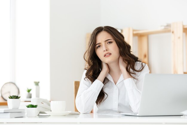 Foto empresaria joven cansada que sufre de mucho tiempo sentado en el escritorio de la computadora en la oficina.