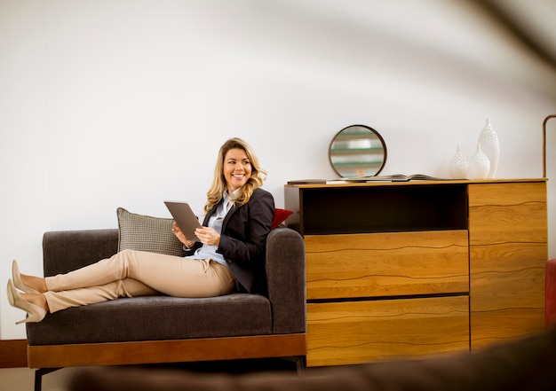 Empresaria joven que descansa con la tableta en el sofá moderno