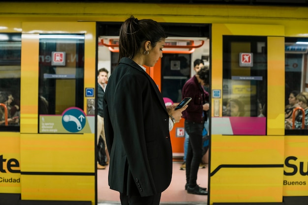 Foto empresaria joven que usa el teléfono móvil que se coloca delante del tren subterráneo