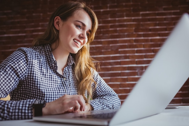 Empresaria joven sonriente del inconformista que usa su computadora en su escritorio en oficina