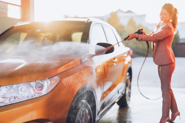 La empresaria lavar el coche en la estación de lavado de coches con máquina de agua a alta presión.