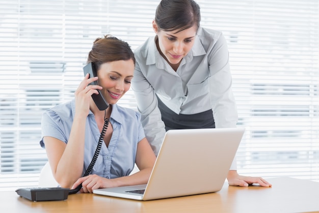 Empresaria llamando y mirando la computadora portátil con colega