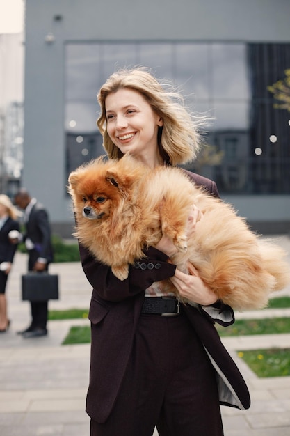 Empresária loira em pé e segurando cachorro na frente do escritório moderno