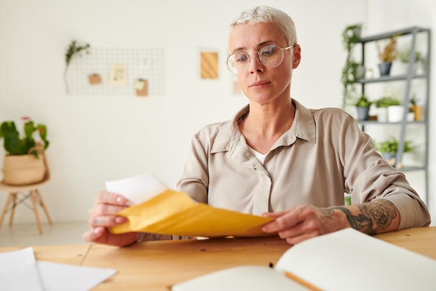 Empresária loira séria em óculos sentado na mesa de escritório e abrindo o envelope com ônibus