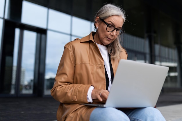 Empresária madura senta-se com um laptop no colo na entrada de um prédio de escritórios