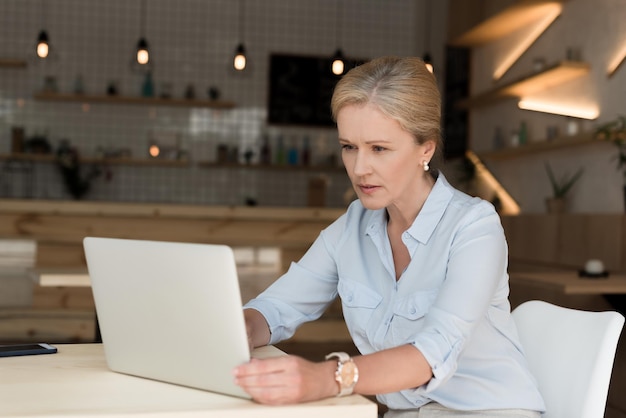 Empresária madura séria usando laptop no café