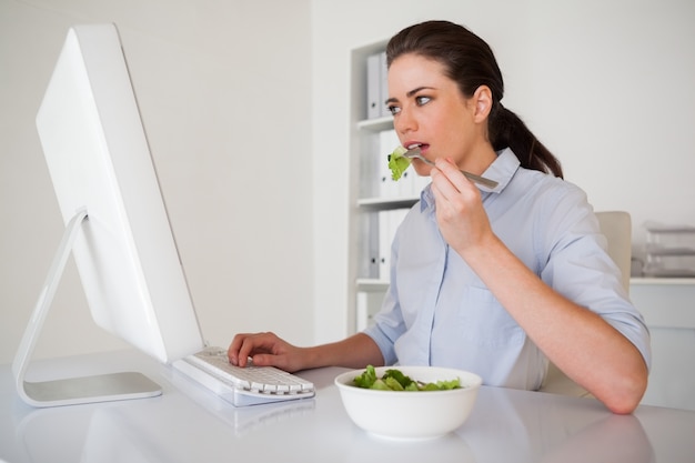 Empresaria morena casual comiendo una ensalada en su escritorio