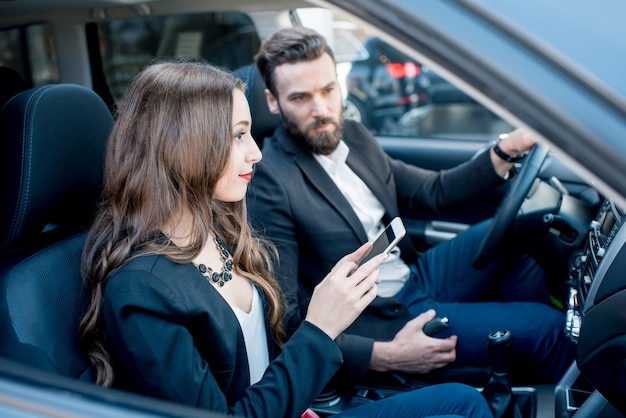 La empresaria mostrando teléfono al empresario sentados juntos en la parte delantera del coche