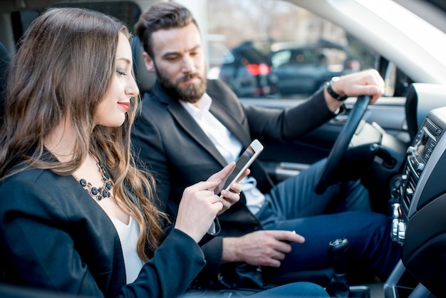 La empresaria mostrando teléfono al empresario sentados juntos en la parte delantera del coche