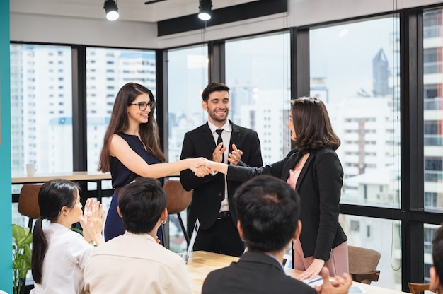 Empresaria multiétnica estrecharme la mano con un acuerdo de cooperación empresarial y compañeros de trabajo felicitando en la oficina moderna