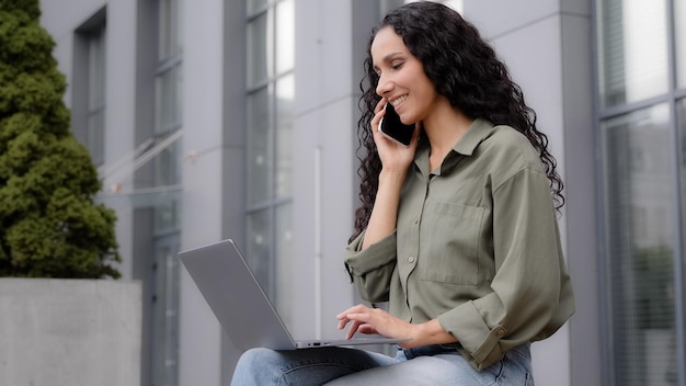 Empresária multitarefa trabalhadora freelancer ao ar livre falando telefone celular digitando laptop
