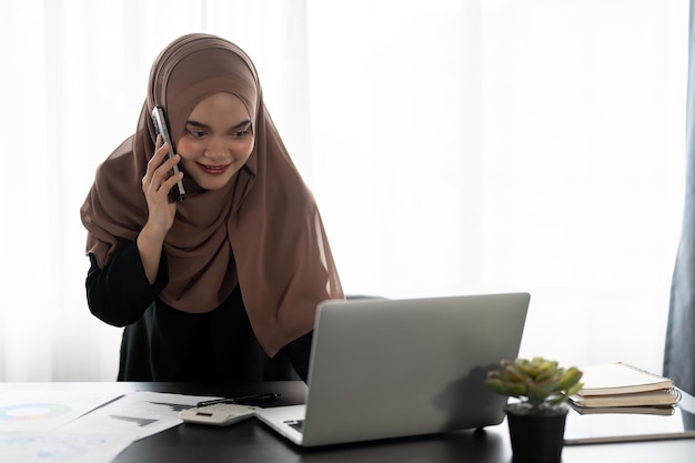 Una empresaria musulmana asiática profesional habla por teléfono mientras trabaja en su oficina