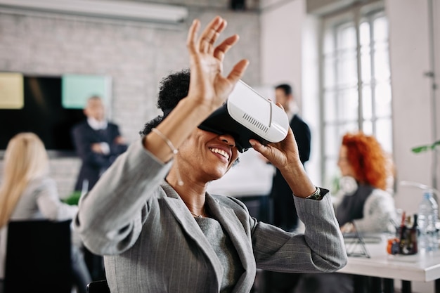 Empresaria negra juguetona probando auriculares de realidad virtual y divirtiéndose en la oficina