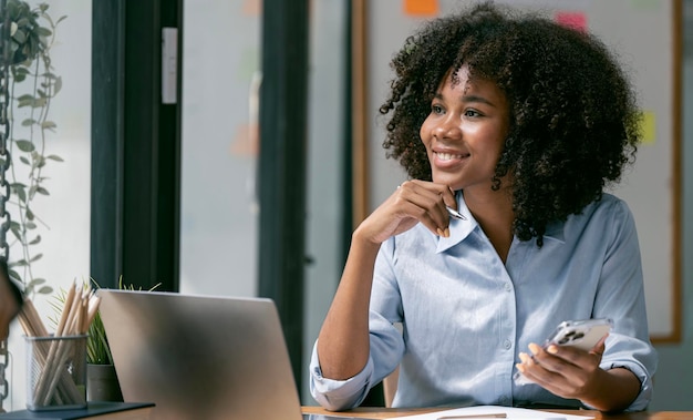 Empresária negra sentada em sua mesa trabalhando em um computador laptop sorrindo bem-sucedida mulher afro-americana trabalhando no escritório