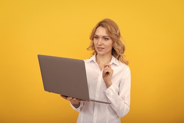 Empresaria ocupada con camisa blanca trabaja en línea con una computadora portátil en un empresario de fondo amarillo
