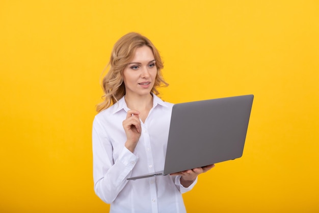 Empresária ocupada em camisa branca trabalha online com laptop em empresário de fundo amarelo