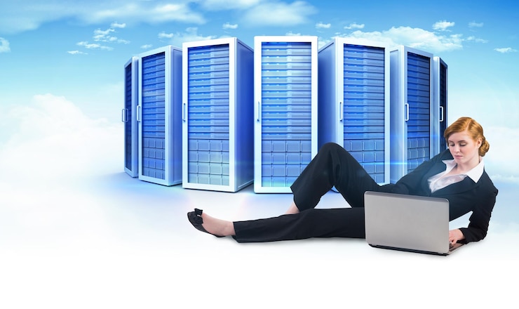 Foto empresaria pelirroja usando su computadora portátil contra una imagen compuesta de torres de servidores