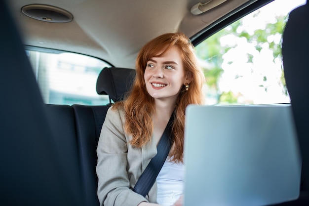 Empresária pensativa com laptop no banco de trás do carro Jovem mulher usando um laptop em um carro