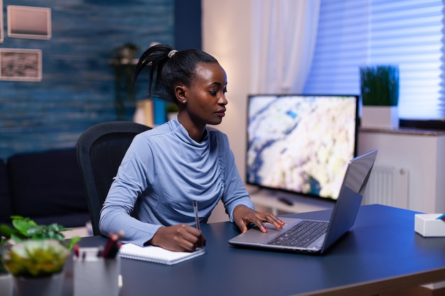 Empresaria de piel oscura que trabaja de forma remota desde la oficina en casa a altas horas de la noche usando la computadora portátil. Empresario negro sentado en el lugar de trabajo personal escribiendo en el teclado.