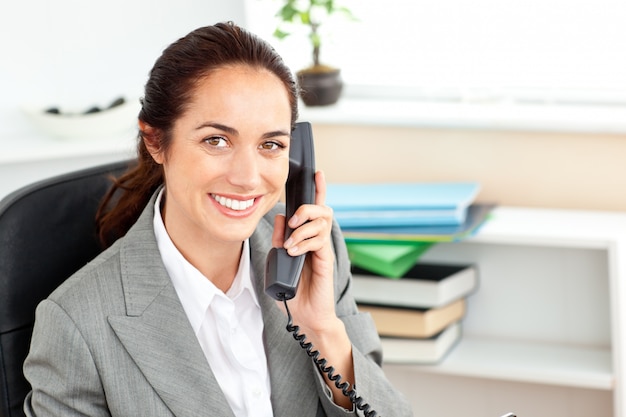 Empresaria positiva hablando por teléfono sentado en su oficina
