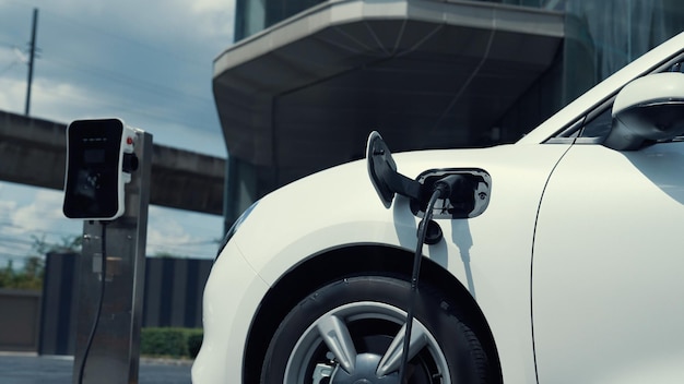 Una empresaria progresista instala el enchufe del cargador desde la estación de carga en su coche eléctrico antes de conducir por el centro de la ciudad Coche recargable ecológico impulsado por energía limpia y sostenible