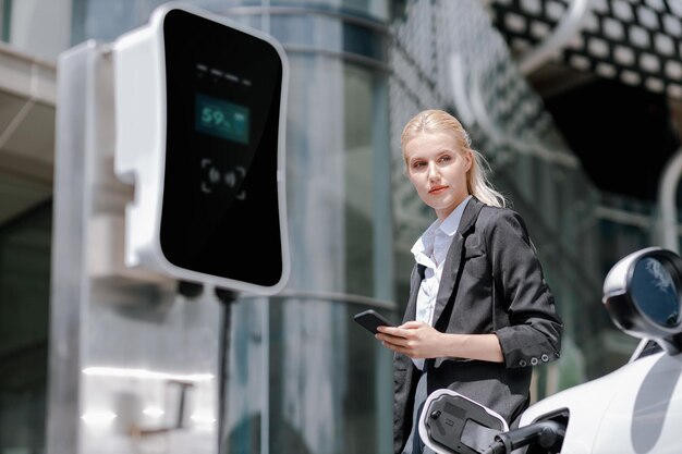 Empresária progressiva com maquete de smartphone com EV na estação de carregamento