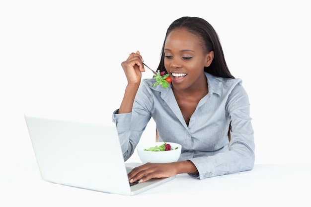 Empresaria que trabaja con una computadora portátil mientras que come una ensalada