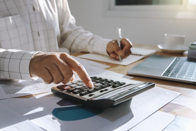 Empresaria que trabaja en el escritorio en la oficina y que usa la calculadora y la computadora portátil con la pluma para calcular