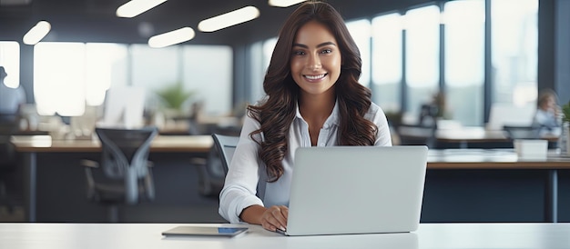 Empresaria que trabaja en el escritorio en la oficina sonriendo a la cámara con espacio vacío en la pantalla del portátil para copiar