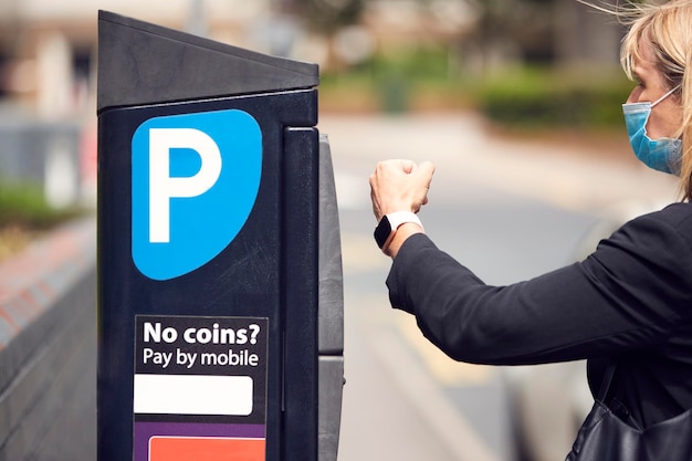 La empresaria que usa una máscara facial PPE realiza un pago sin contacto para el estacionamiento de automóviles con un reloj inteligente