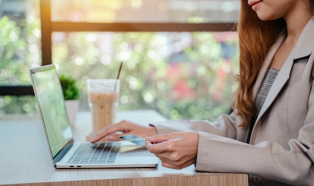 Empresaria que usa tarjeta de crédito para compras en línea. Mujer con tecnología en computadora en café sola.