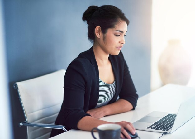 Empresaria de redes sociales con computadora portátil y en su escritorio en una oficina de trabajo moderna con un destello de lente Comunicación en línea o conectividad tecnológica y persona femenina en su espacio de trabajo