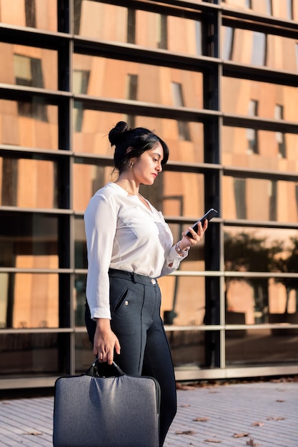 La empresaria revisando su teléfono frente a un edificio de oficinas en el distrito financiero, concepto de empresario exitoso y estilo de vida urbano